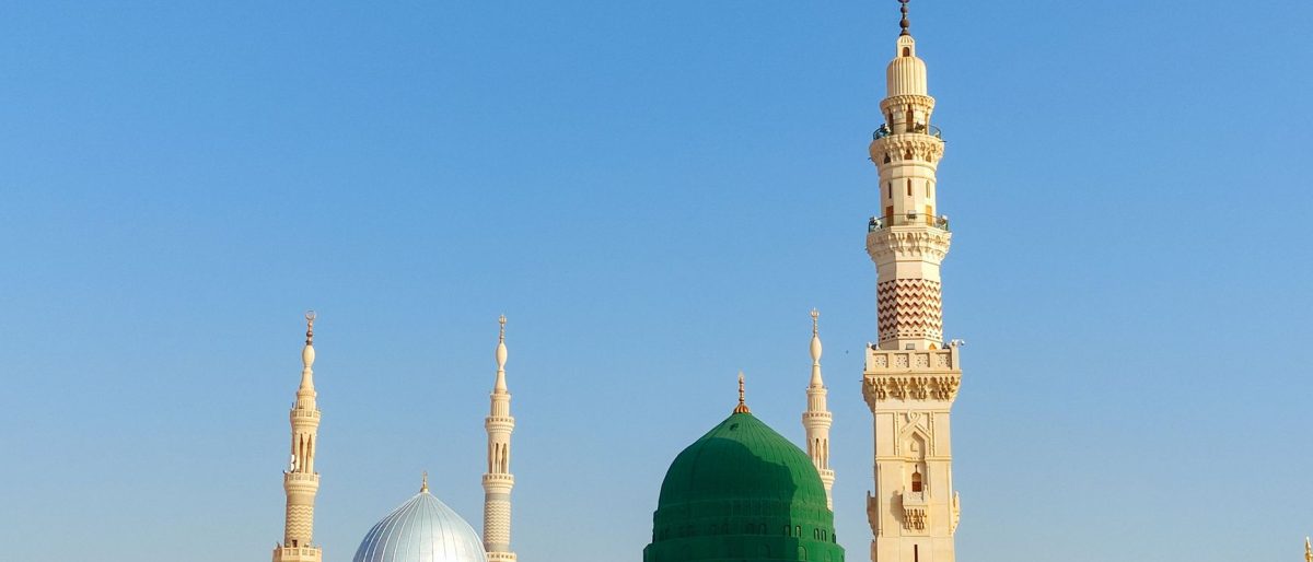 Scenic view of the Prophet's Mosque in Medina, showcasing its iconic minarets and dome under a clear blue sky.