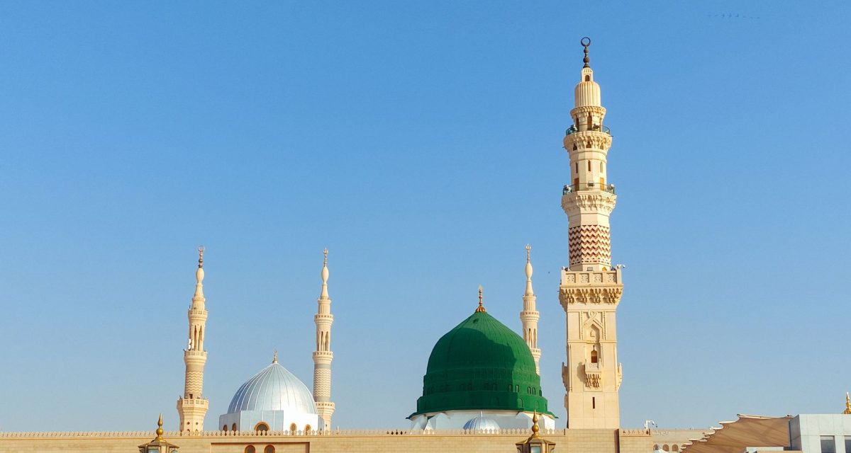 Scenic view of the Prophet's Mosque in Medina, showcasing its iconic minarets and dome under a clear blue sky.