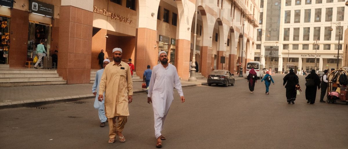 People walking on a bustling street in Makkah, showcasing traditional attire and Middle Eastern architecture.