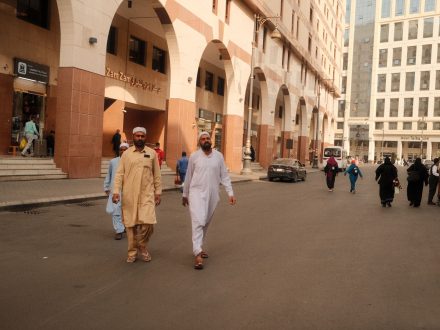 People walking on a bustling street in Makkah, showcasing traditional attire and Middle Eastern architecture.